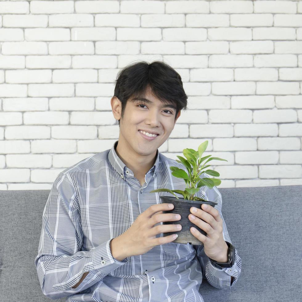 um jovem asiático segura um vaso de plantas e está sorrindo brilhantemente. foto
