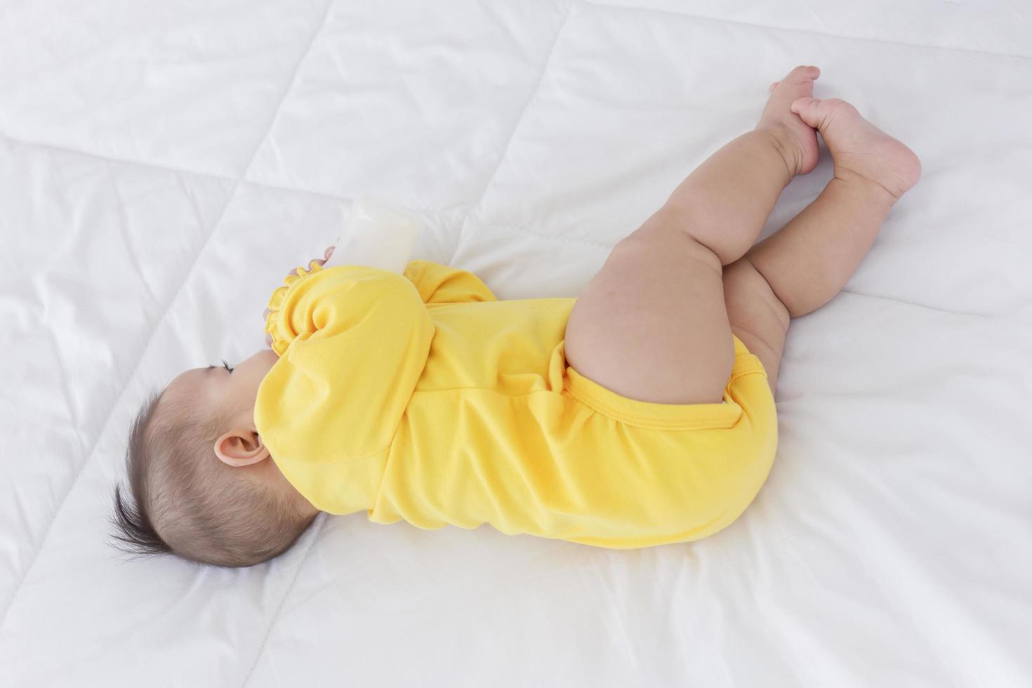 um bebê asiático está dormindo na cama e chupando o leite engarrafado. foto