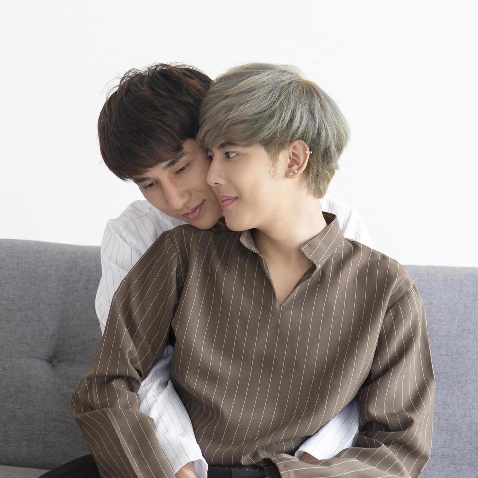 um casal masculino com um homem asiático abraçado no sofá com seu amor um pelo outro. foto