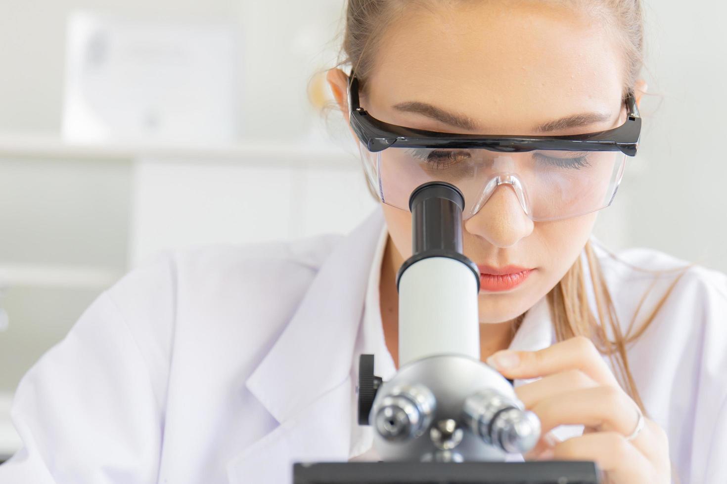 belas cientistas femininas estão olhando para os microscópios em um laboratório de ciências com vários equipamentos no laboratório. foto