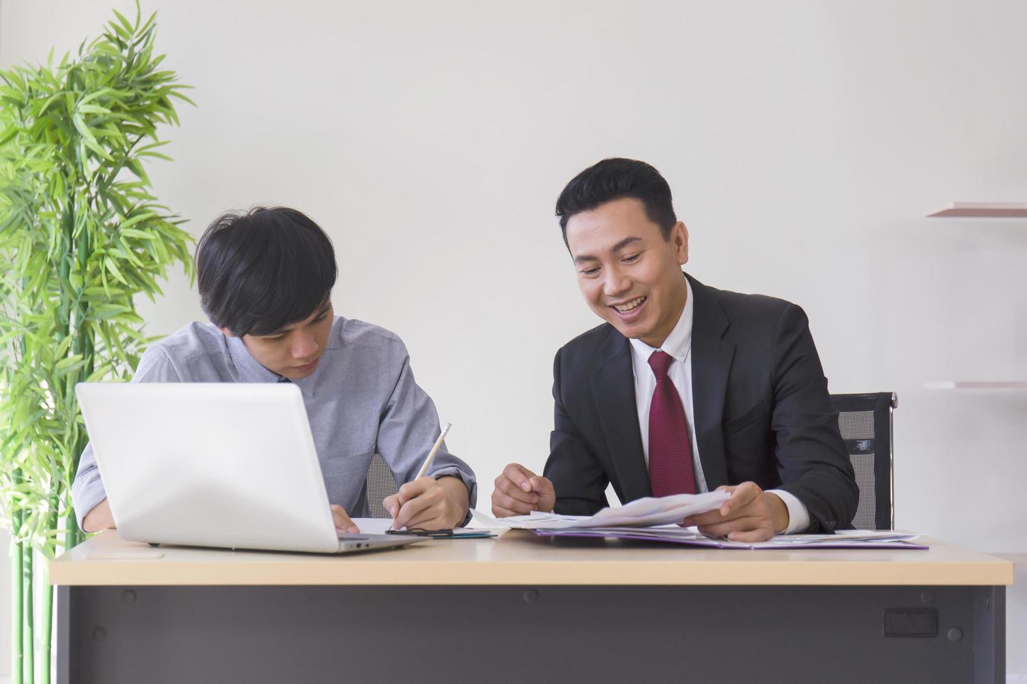 um supervisor masculino asiático ensina o recém-chegado ao escritório em sua mesa. foto