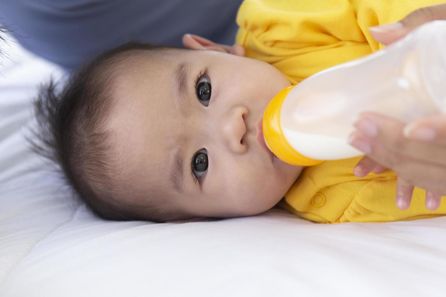 um bebê asiático é alimentado com mamadeira na cama. foto