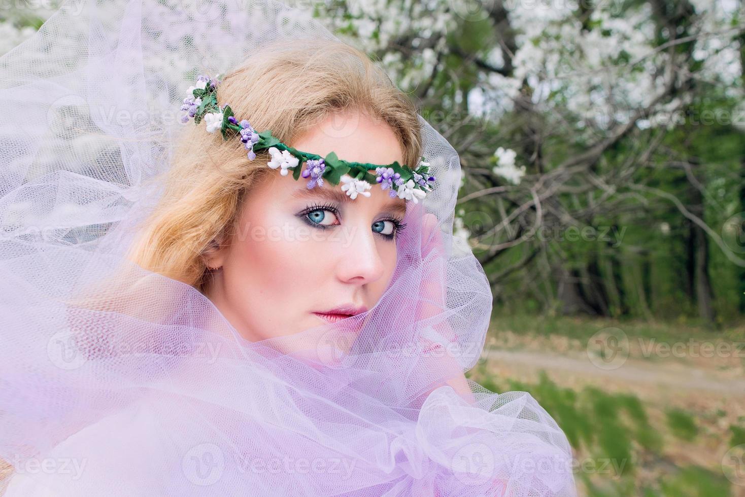 bela jovem loira na coroa de flores florescendo árvores na primavera foto