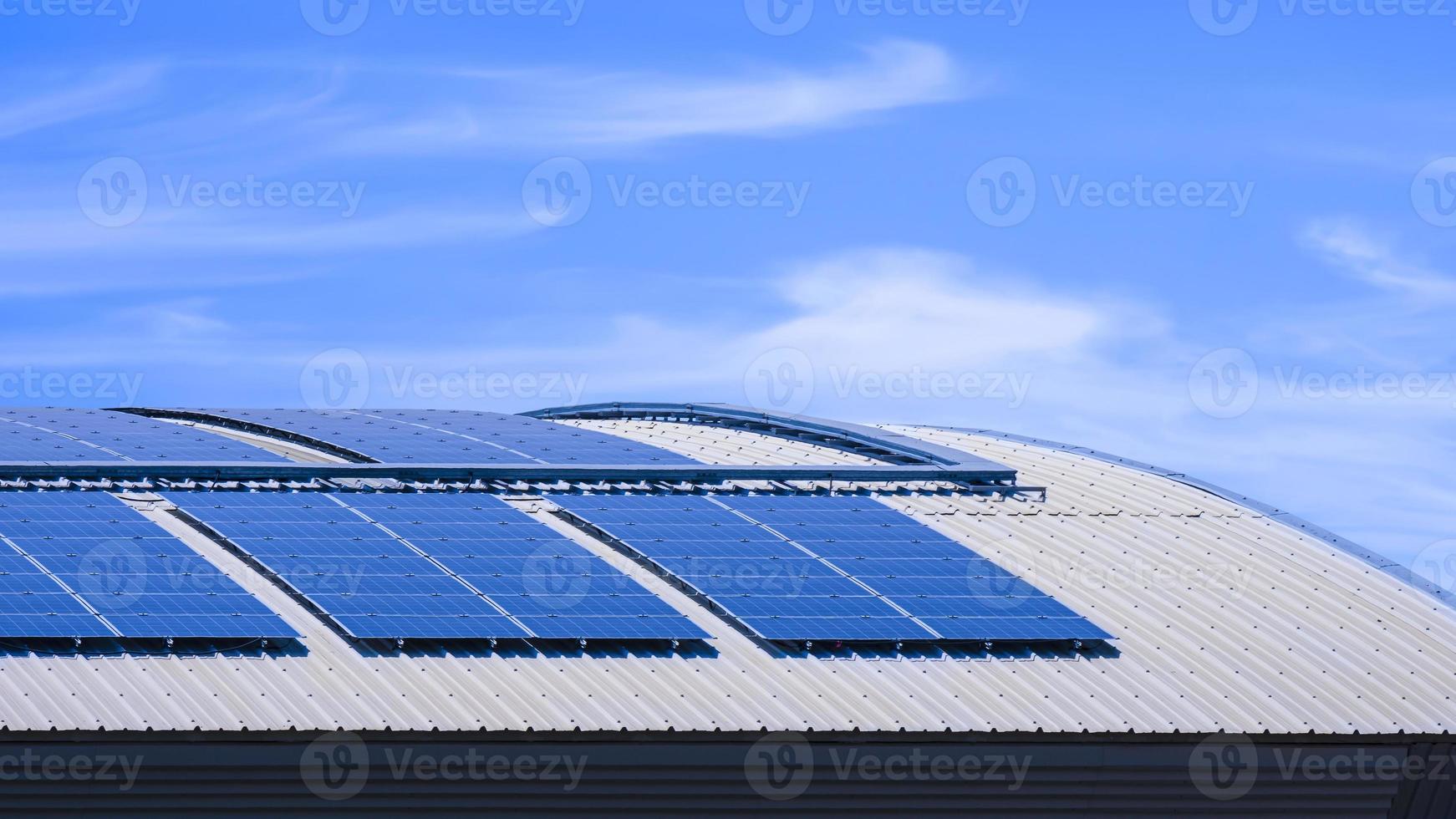 muitos painéis solares em cima do telhado de aço curvo do edifício industrial contra o fundo do céu azul foto