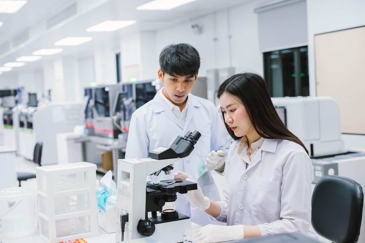 dois cientistas médicos trabalhando em laboratório médico, jovem cientista feminina olhando para o microscópio. selecione o foco na jovem cientista foto