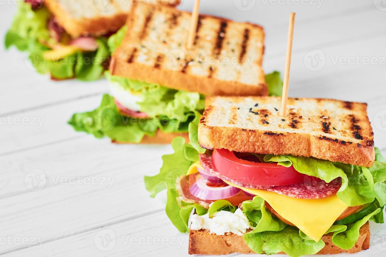 três sanduíches com presunto, alface e legumes frescos em um fundo branco foto