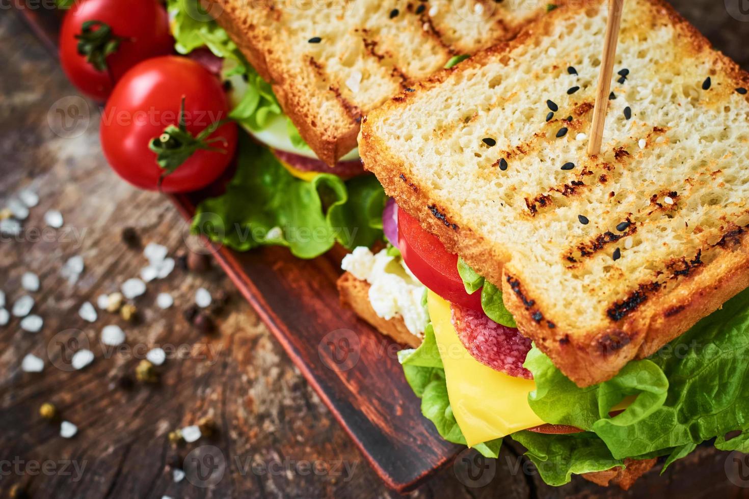 sanduíche caseiro com presunto, alface, queijo e tomate em um fundo de madeira foto