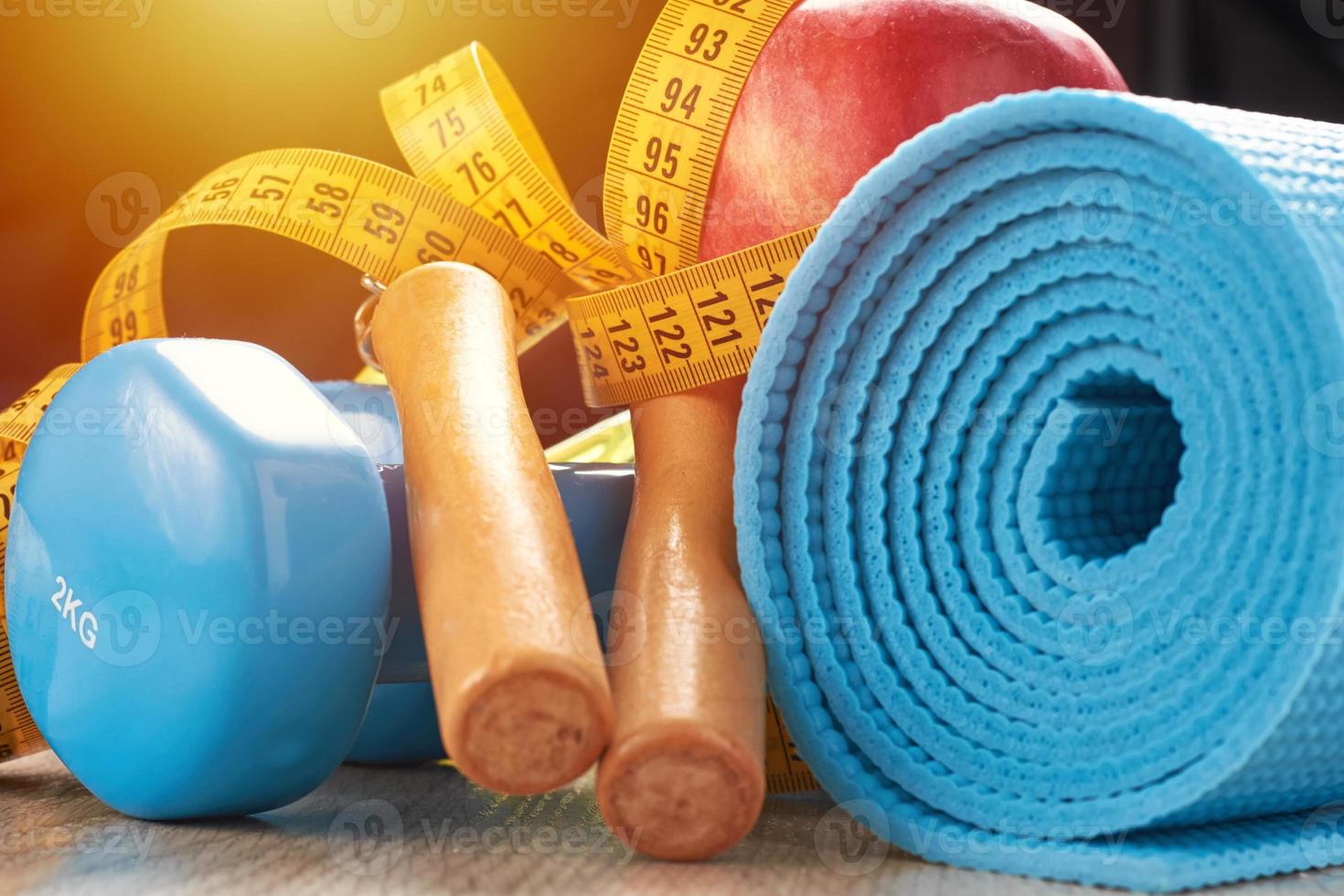 conceito de fitness com halteres azuis, tapete de fitness e pular corda em um fundo escuro foto