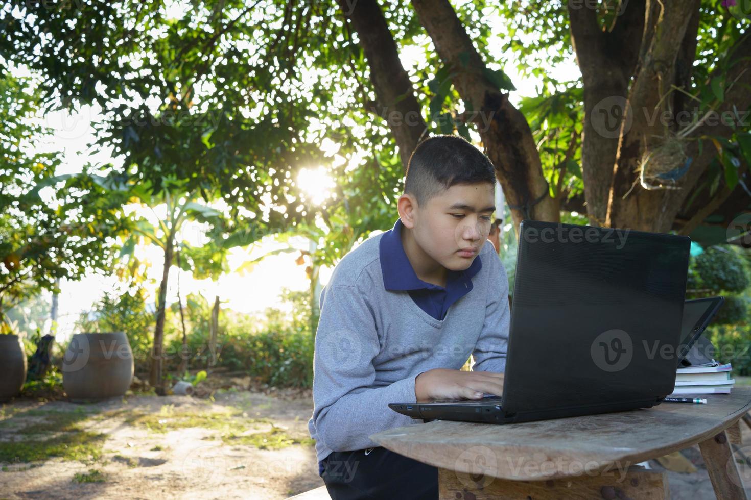 menino está estudando on-line em uma mesa de madeira com um laptop e tablet durante as horas da manhã em uma casa rural. conceito área rural de educação on-line e trabalho em casa foto