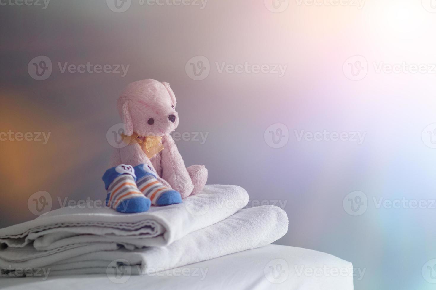 imagem borrada, um ursinho de pelúcia rosa de cabelo curto estava deitado em uma toalha branca no colchão da cama da janela pela manhã, enquanto um ursinho de pelúcia se preparava para sua filha brincar antes de tomar banho. foto