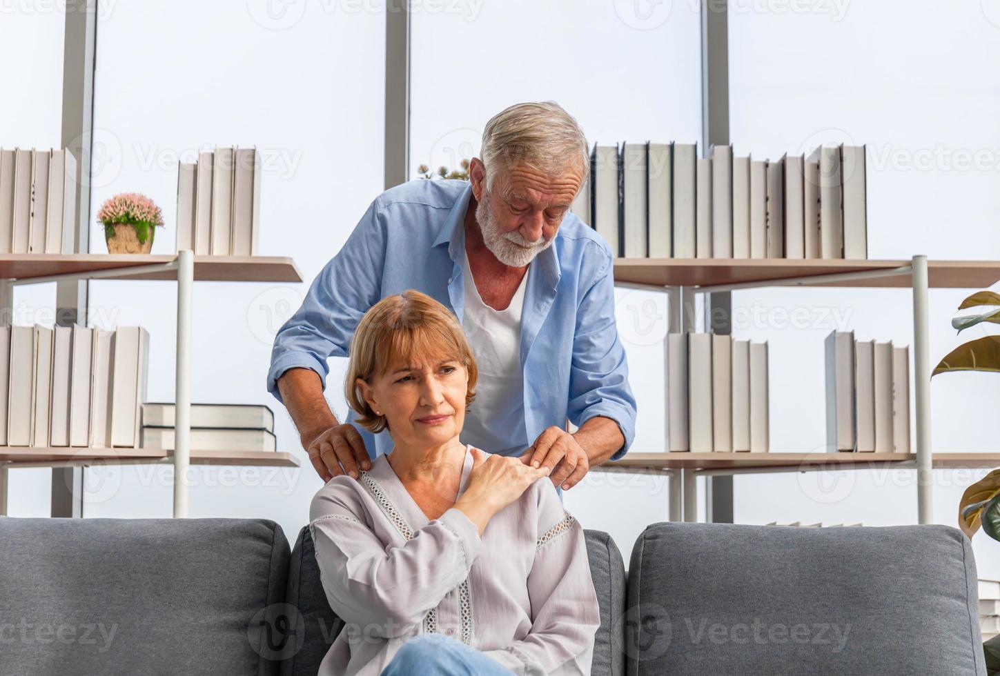 retrato de casal sênior na sala de estar, mulher madura com dor no ombro. dor no braço superior, dor e lesão no pescoço e ombro da mulher foto