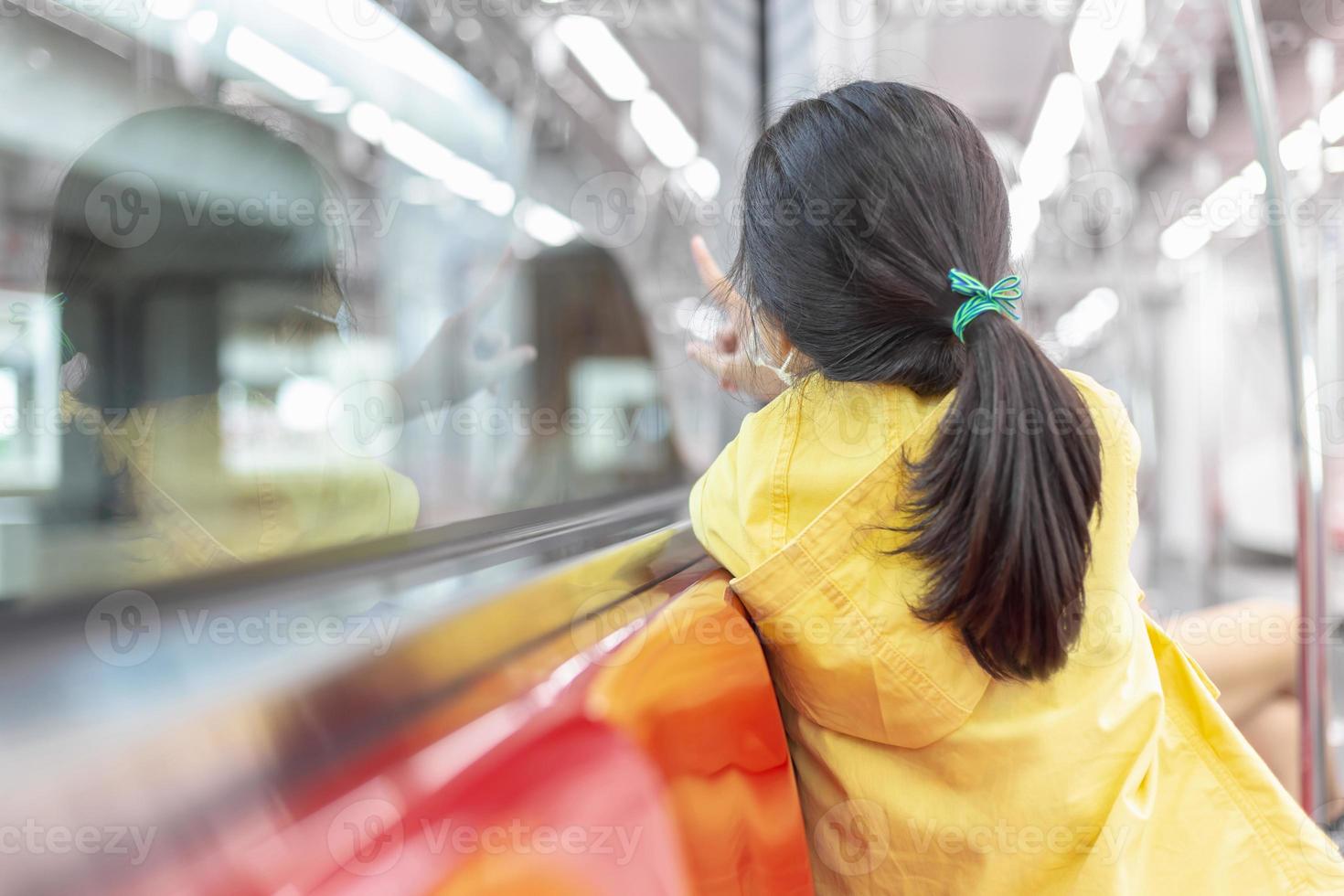 garota olhando pela janela do trem lá fora, enquanto se move. criança usa máscara facial durante surto de coronavírus e gripe, viajando de trem. foto