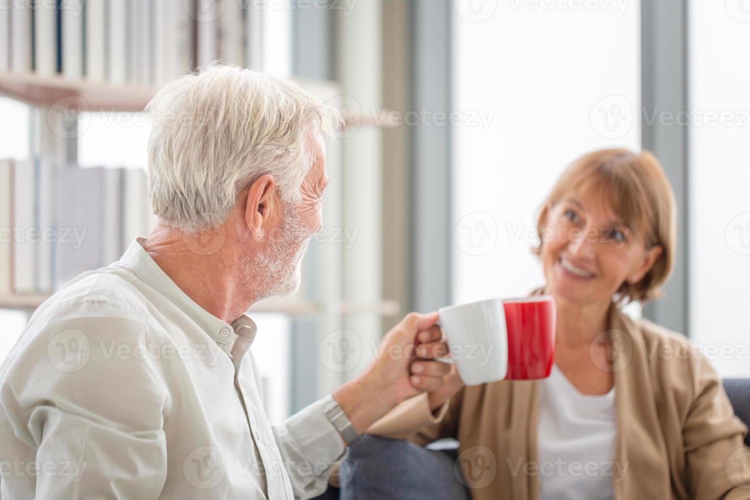 homem sênior e mulher segurando xícaras de café na sala de estar, casal sênior dentro de casa durante uma pausa para o café foto