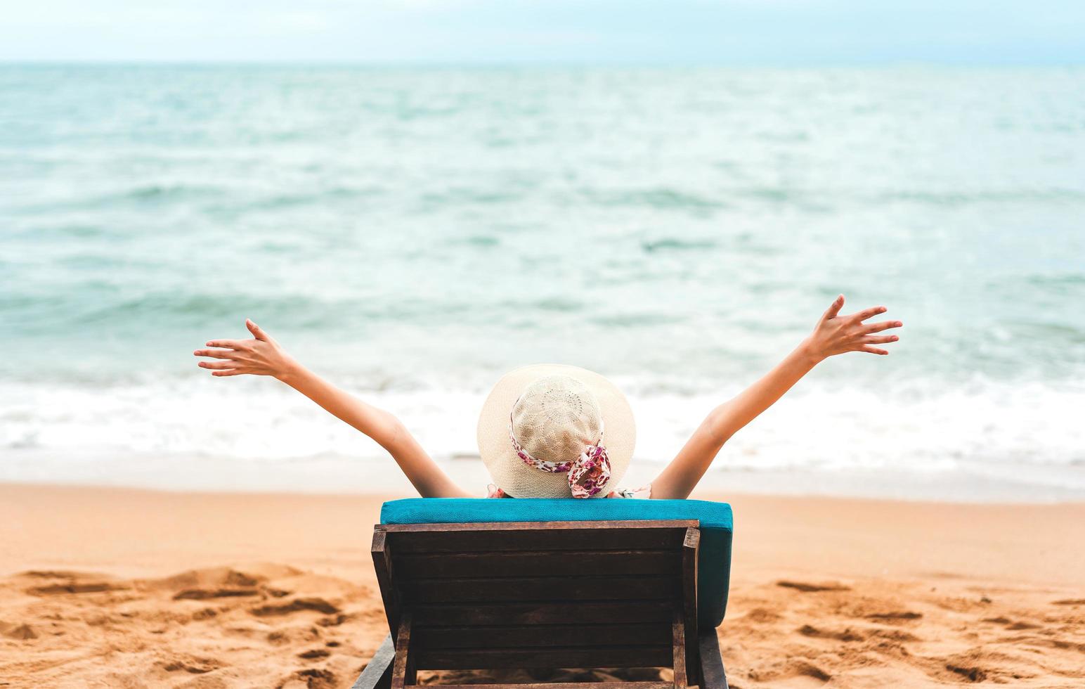 jovem mulher da ásia relaxando na cadeira de praia braço para cima a mão com chapéu flexível foto