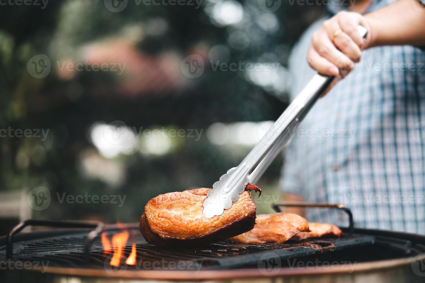 mão de homem grelhando churrasco em chamas no quintal no dia foto