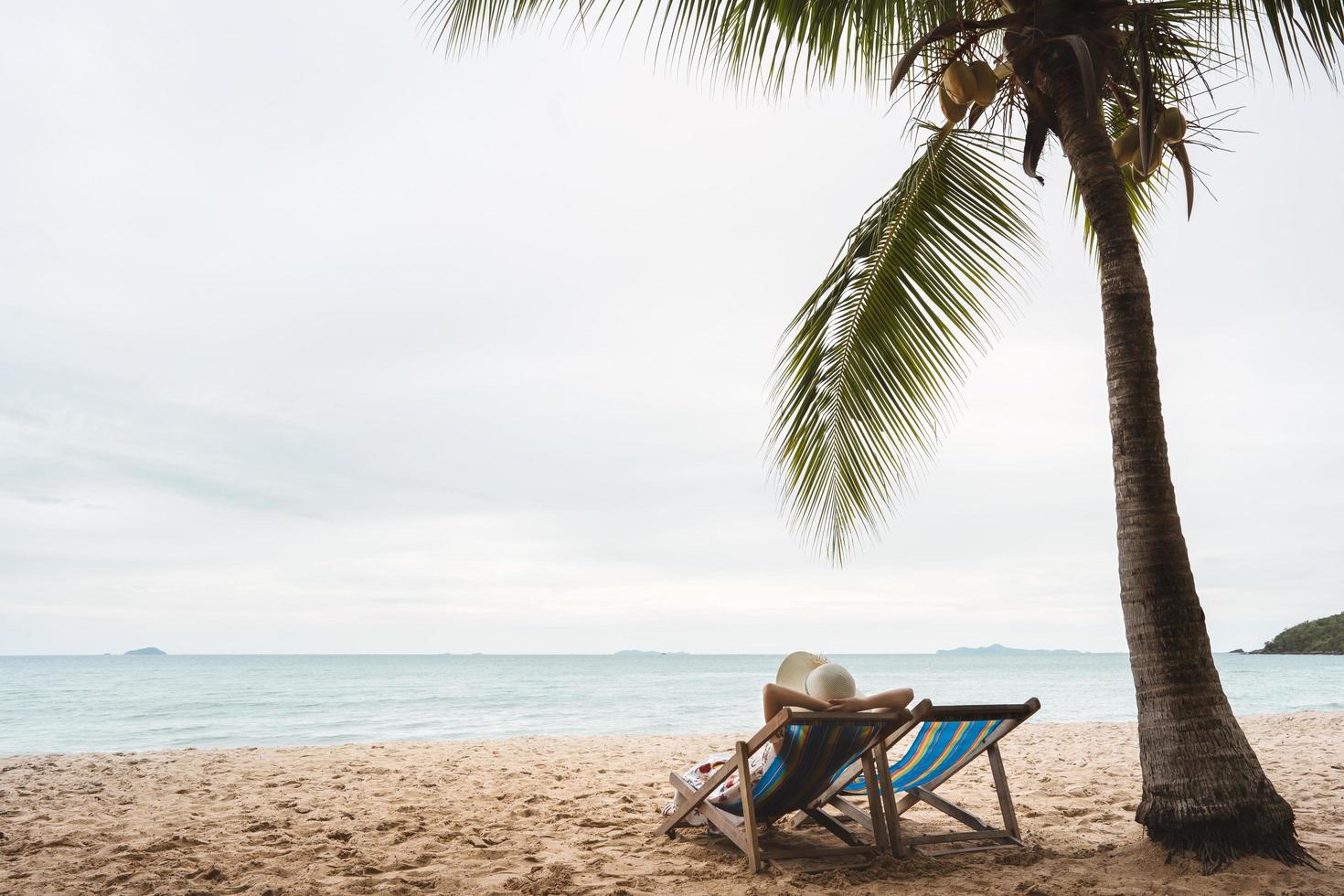 mulher asiática na cadeira de praia sob palmeira tropical foto