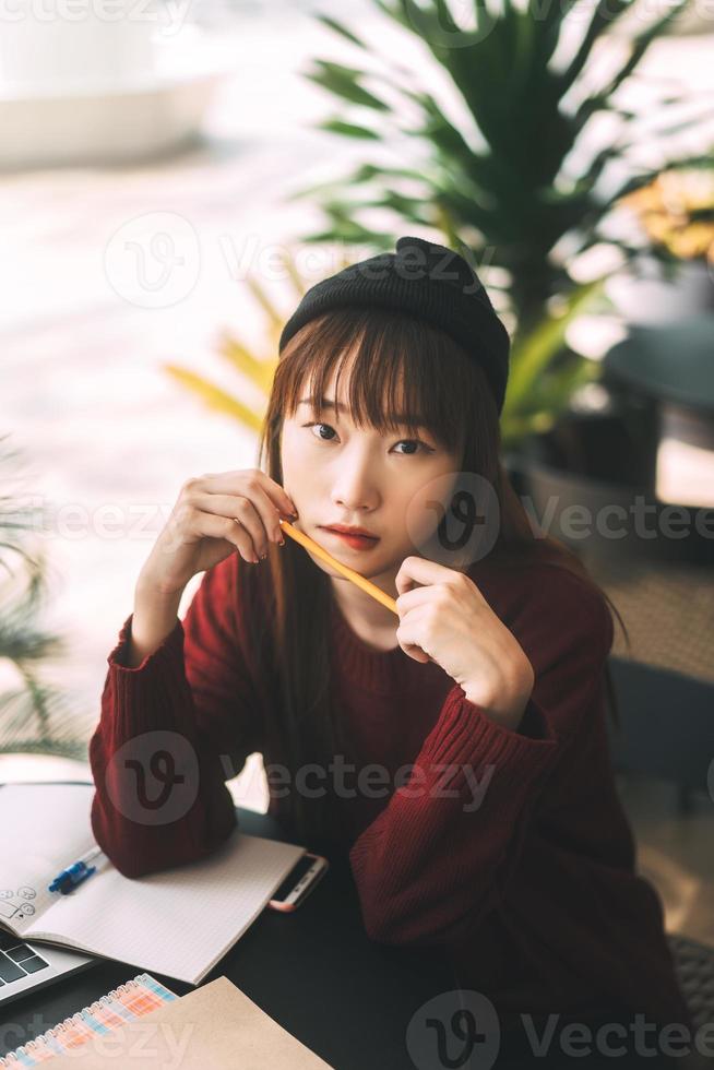 retrato de mulher jovem estudante universitário asiático adulto com laptop para estudo no café em dia de inverno. foto