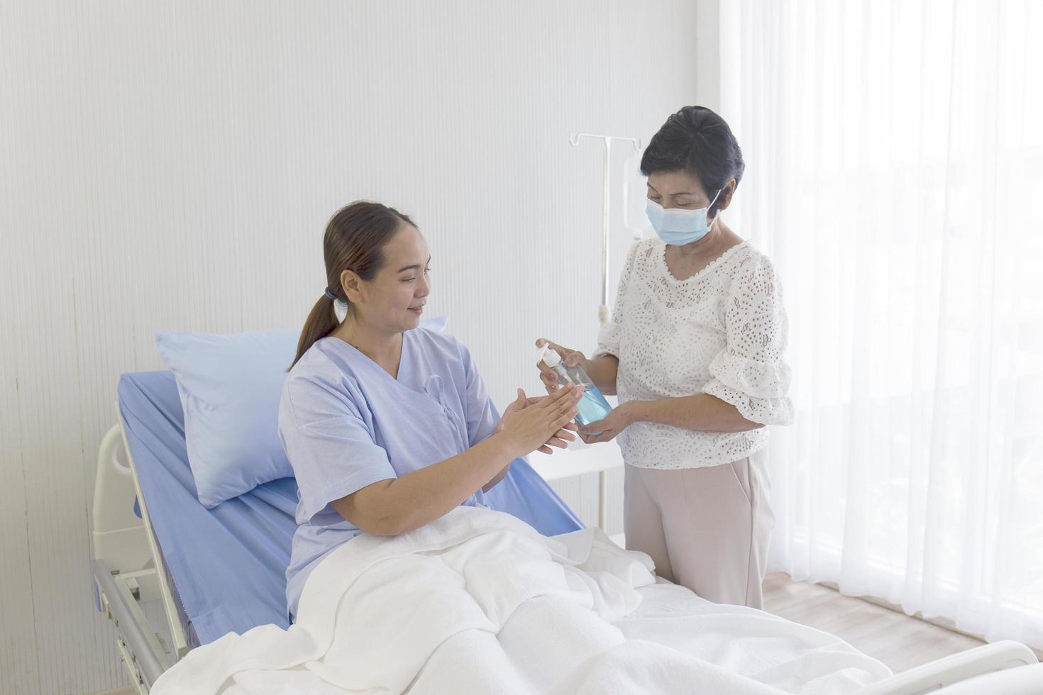 uma jovem asiática que estava doente em um hospital estava deitada em uma cama de recuperação. a mãe, que cuidava do lado dela, estava usando álcool gel para lavar as mãos. foto