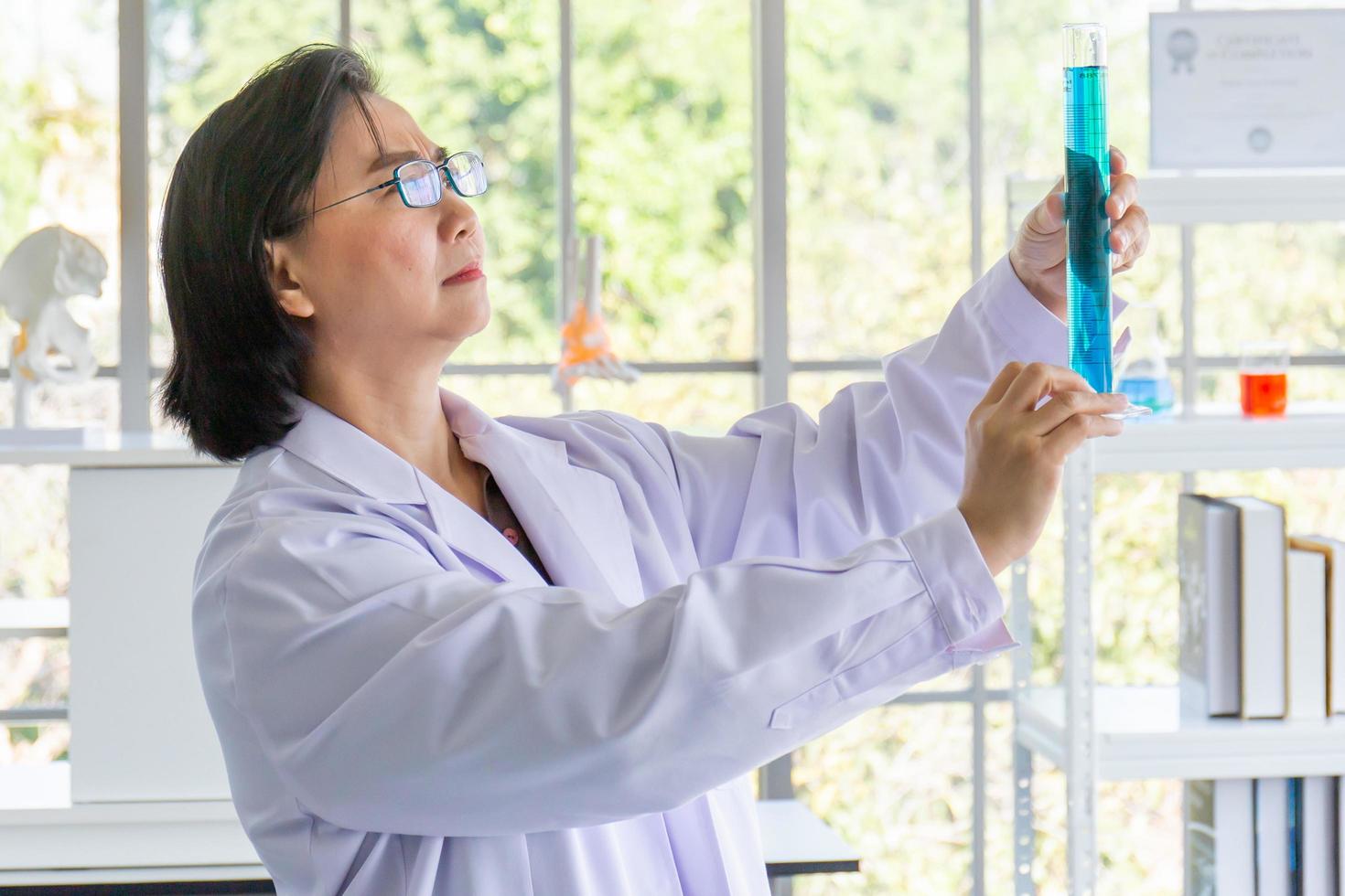 descobrindo uma cura para uma cientista asiática que está concentrada, segurando um tubo de ensaio e assistindo enquanto trabalha. foto