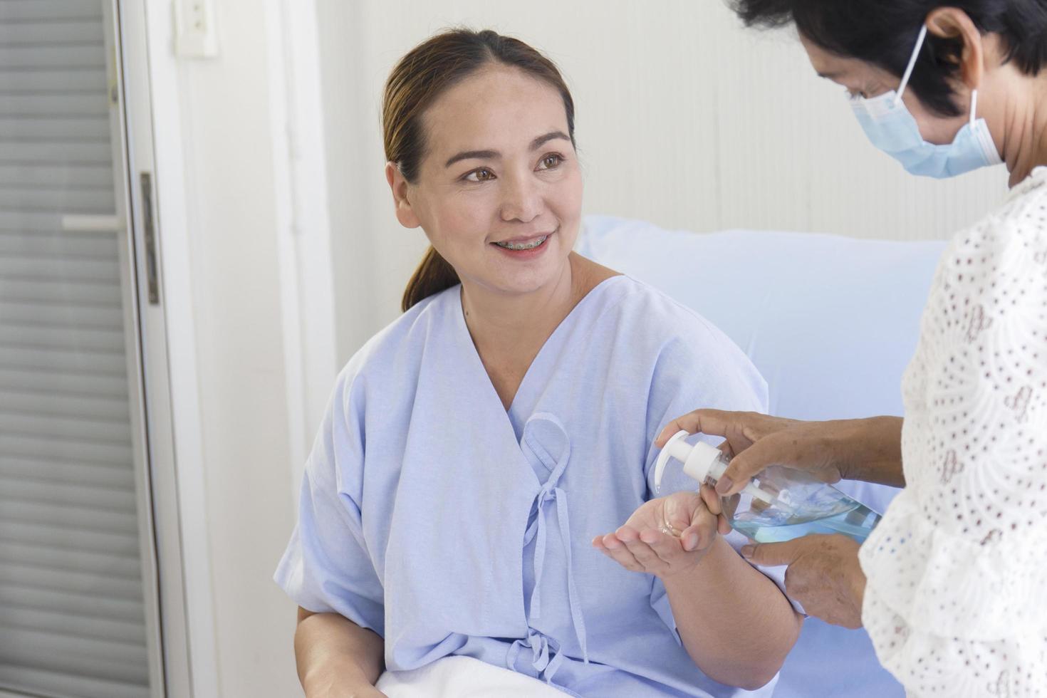 uma jovem asiática que estava doente em um hospital estava deitada em uma cama de recuperação. a mãe, que cuidava do lado dela, estava usando álcool gel para lavar as mãos. foto