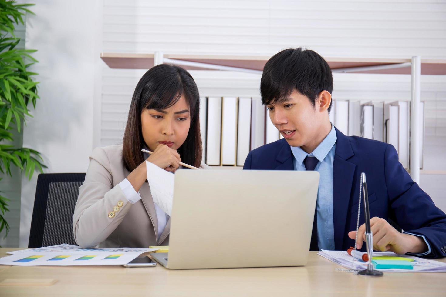 dois funcionários asiáticos masculinos e femininos ajudaram a planejar uma mesa cheia de documentos e tablets, notebooks. foto