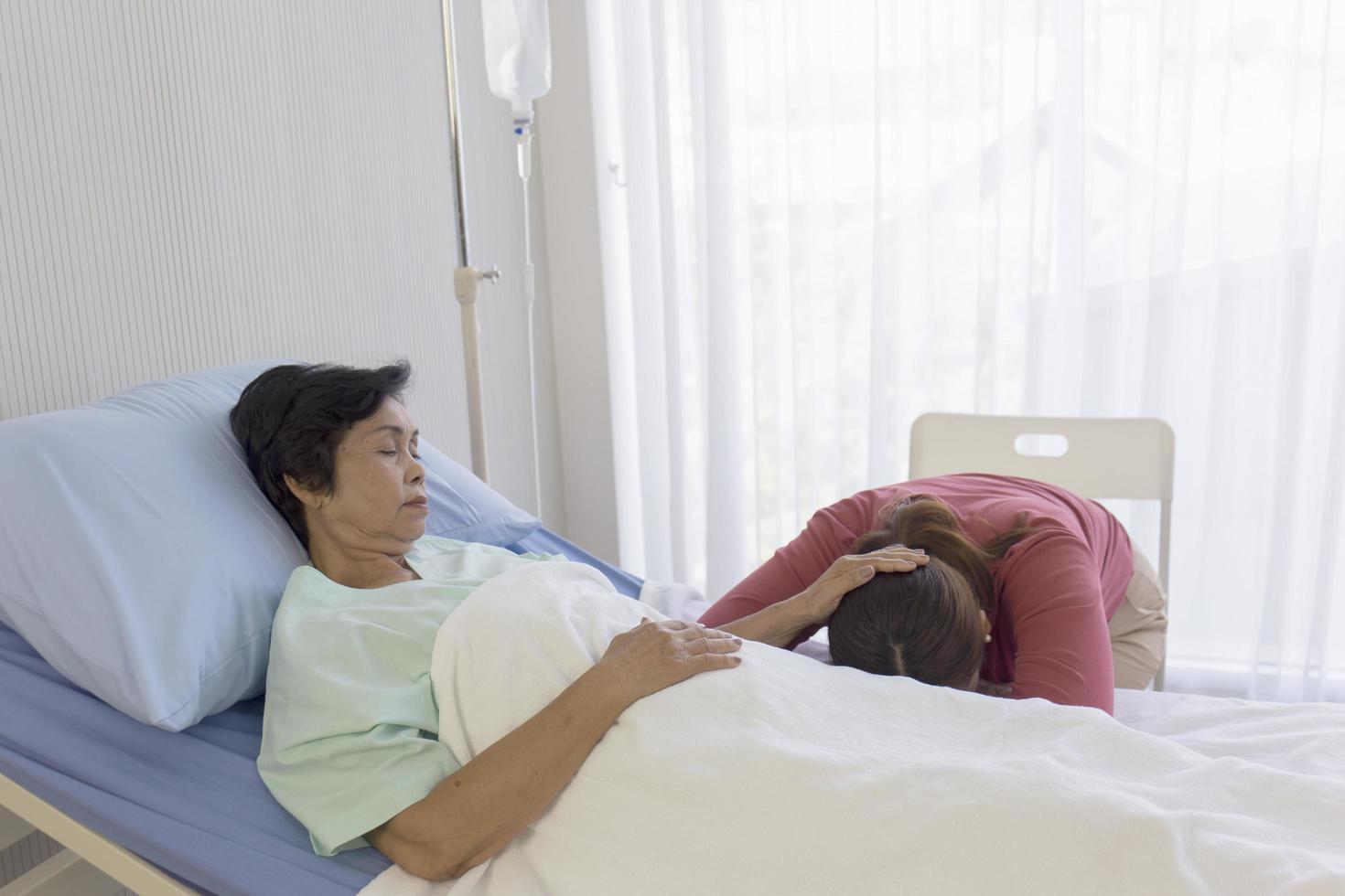 uma mãe doente na cama, mulher asiática esfregou a cabeça da filha dormindo na cama do hospital foto