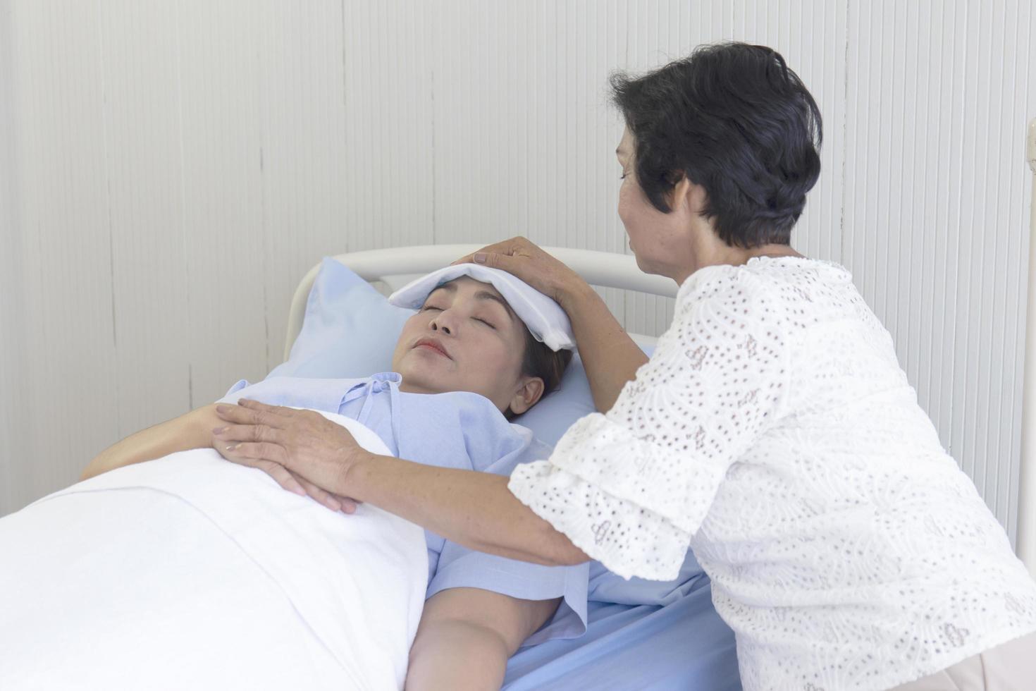 uma mãe asiática cuida de sua filha doente em uma cama de hospital. foto