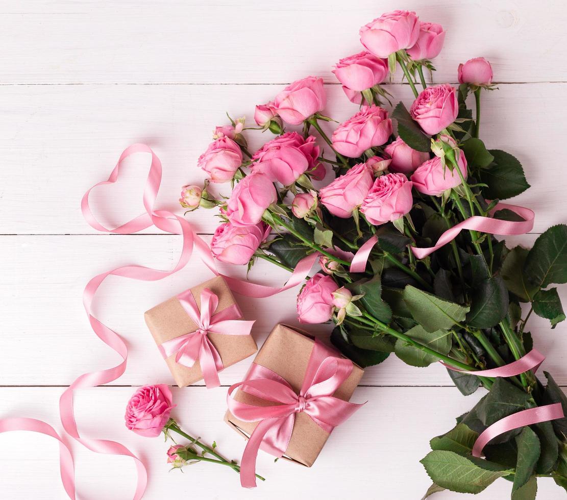 rosas suaves pastel frescas e caixas de presente embrulhadas em papel kraft com fitas na mesa de madeira branca. foto