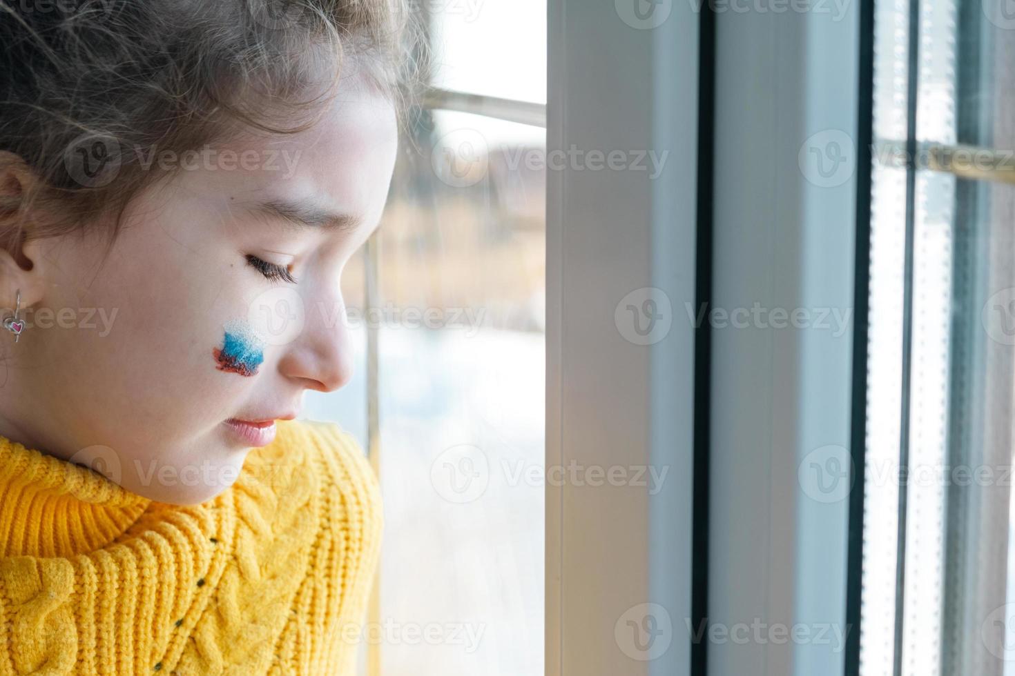 uma criança triste na janela com a bandeira da rússia, se preocupa com lágrimas nos olhos. conflito entre rússia e ucrânia, medo foto