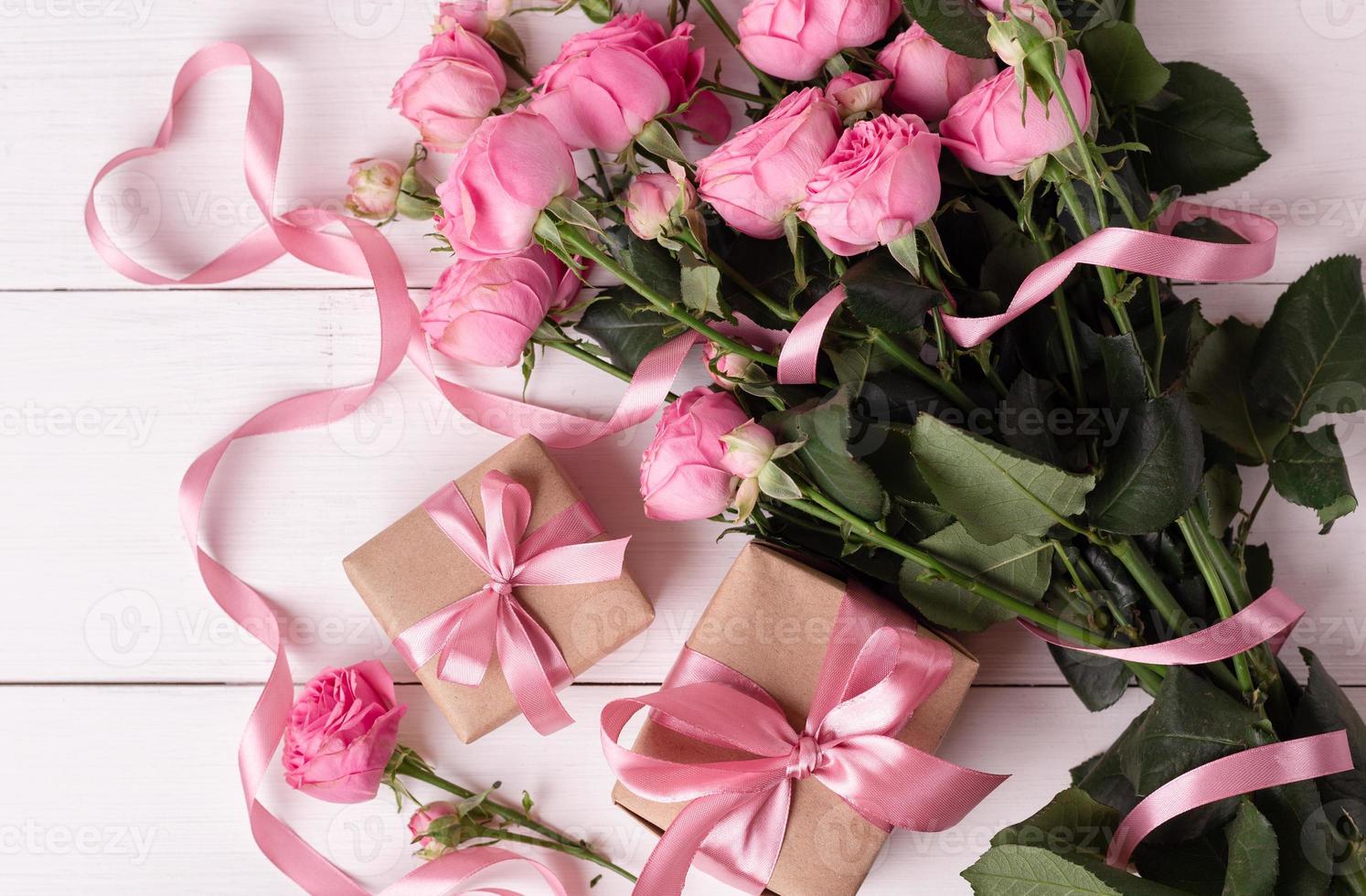 rosas suaves pastel frescas e caixas de presente embrulhadas em papel kraft com fitas na mesa de madeira branca. foto