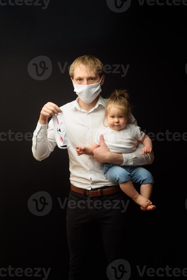 pai em uma máscara médica segura sua filhinha. o conceito de proteger as crianças durante a epidemia de coronavírus foto