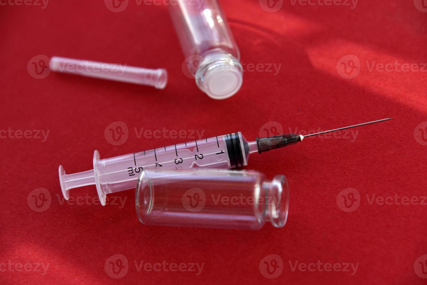 comprimidos de seringa médica e bolhas de vidro em um fundo vermelho foto