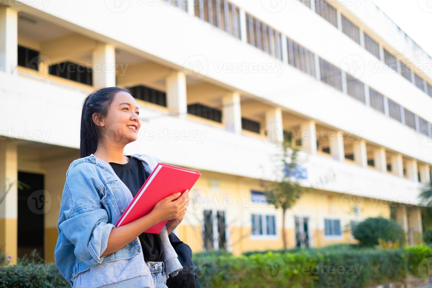 menina sorriso segure o livro-de-rosa em pé no fundo do edifício, de volta à escola. foto