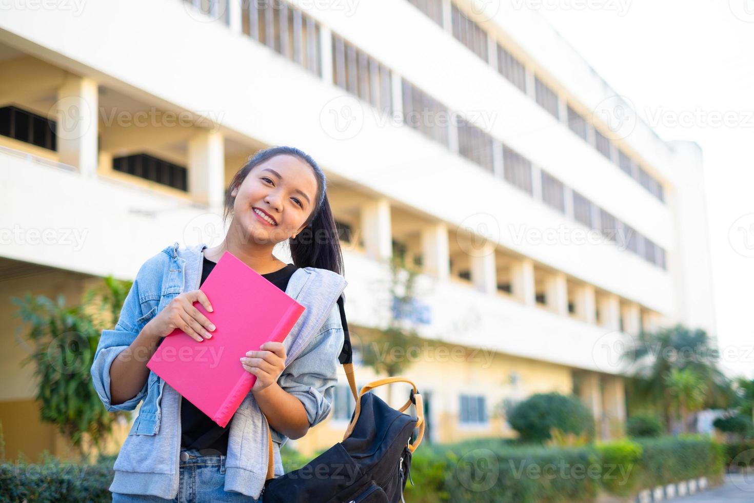 menina sorriso segure o livro-de-rosa em pé no fundo do edifício, de volta à escola. foto