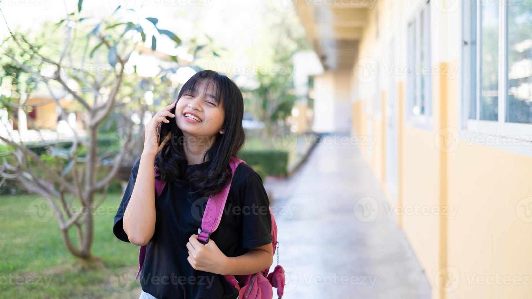 linda jovem usando telefone inteligente na escola, menina asiática, fundo laranja. foto