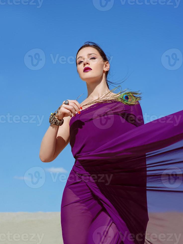 incrível linda mulher morena com a pena de pavão em tecido roxo no deserto. oriental, indiano, moda, conceito de estilo foto
