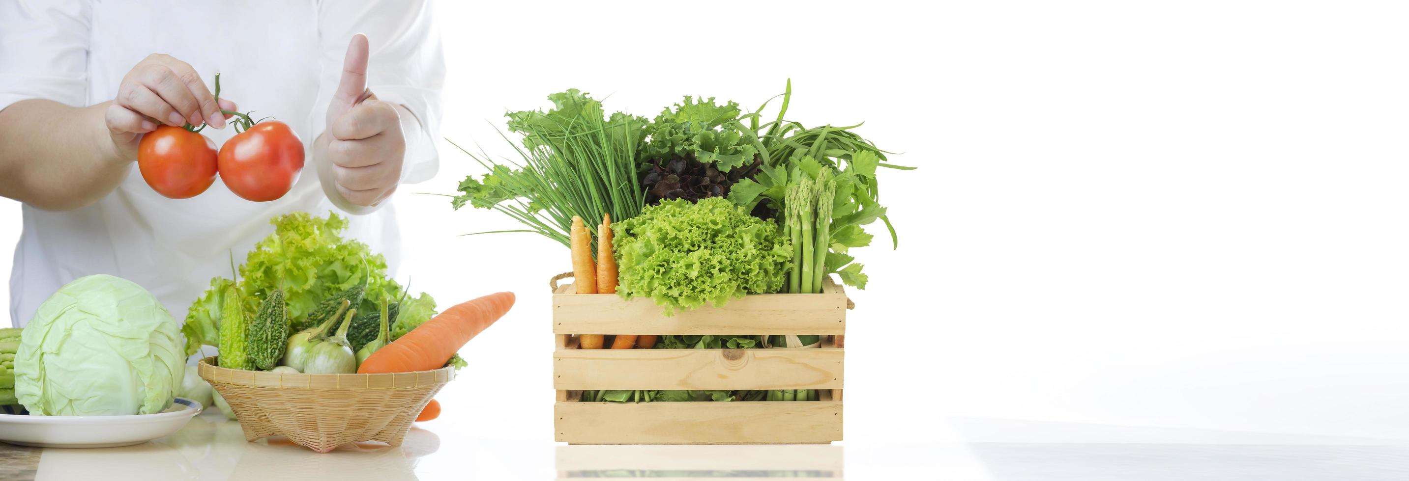 banner de fundo de comida saudável de mulher com excesso de peso segurando tomates frescos e aparecendo o polegar com vários vegetais orgânicos na cesta de bambu e caixa de madeira na mesa de mármore na cozinha branca foto