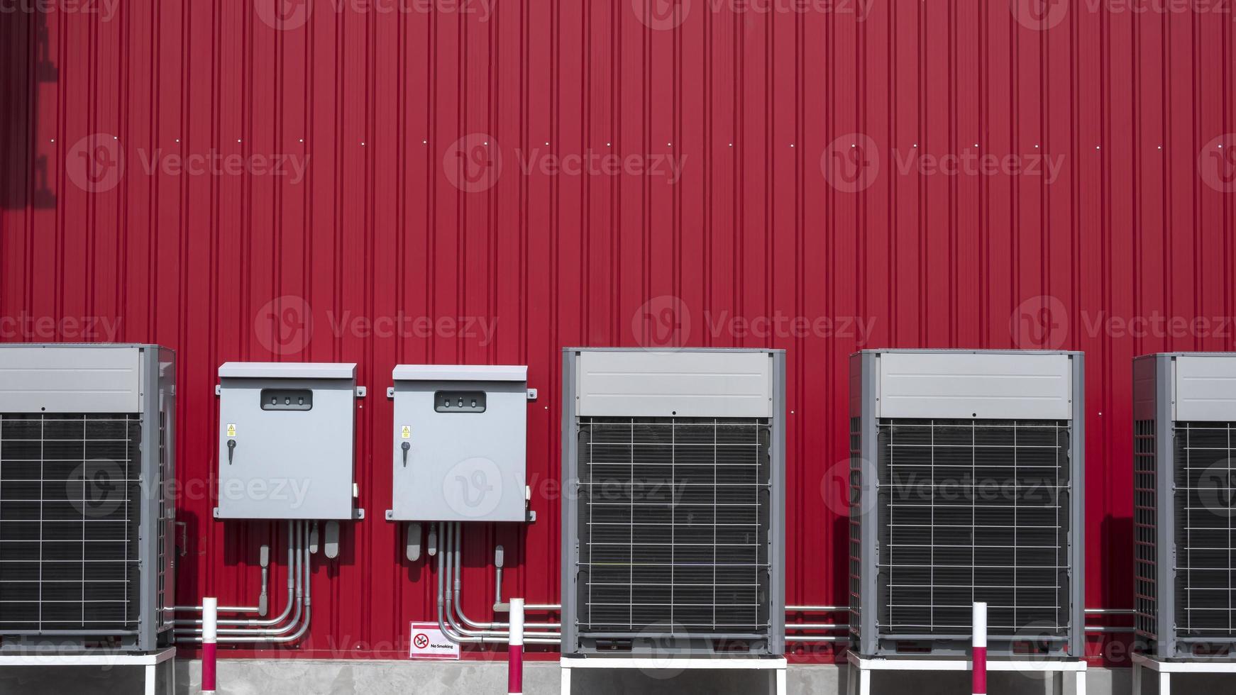 linha de compressores de ar condicionado com 2 armários de controle elétrico e sistema de tubulações elétricas na parede de chapa vermelha fora do edifício foto