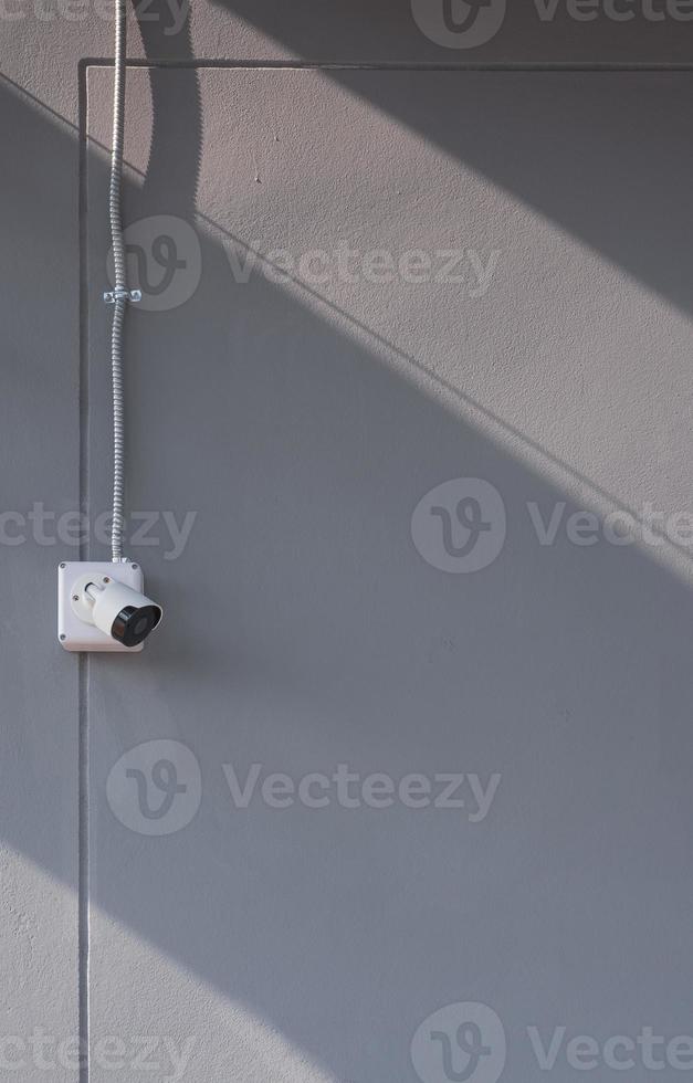 luz solar e sombra na superfície da câmera de segurança com conduíte de metal flexível na parede de cimento cinza em quadro vertical foto