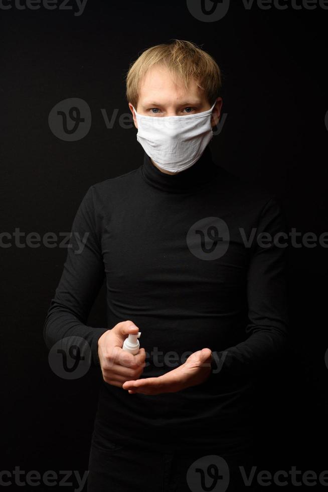um retrato de homem com máscara facial médica usando spray desinfetante nas mãos. conceito de pessoas, medicina e saúde. proteção contra o coronavírus foto