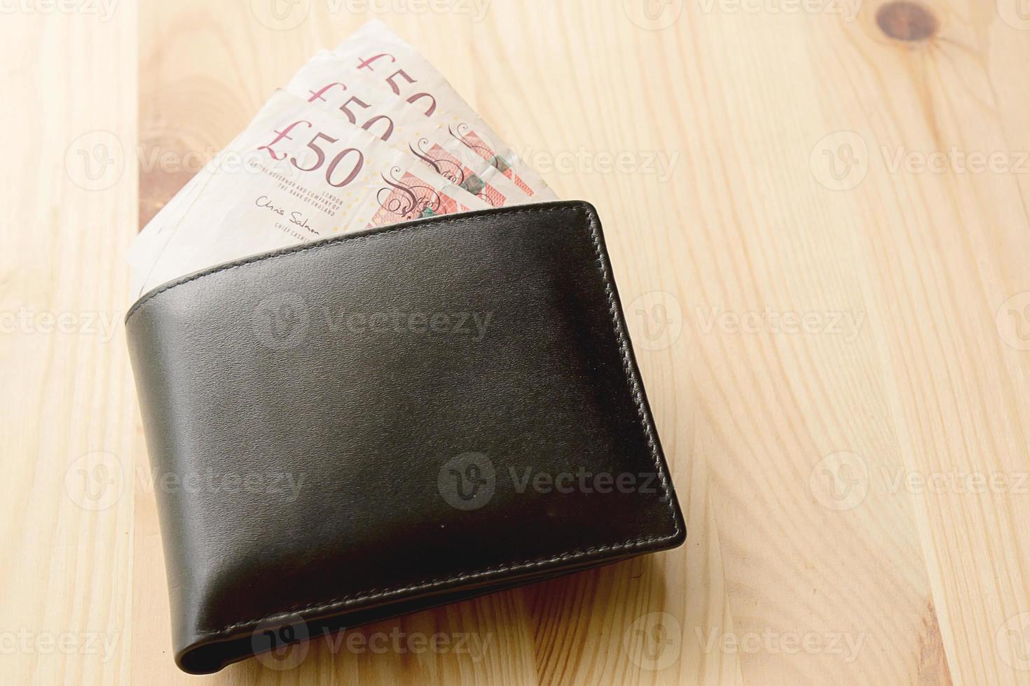 vista de alto ângulo da carteira masculina de couro preto moderno com dinheiro de libra no antigo plano de fundo texturizado de madeira áspera com espaço de cópia foto