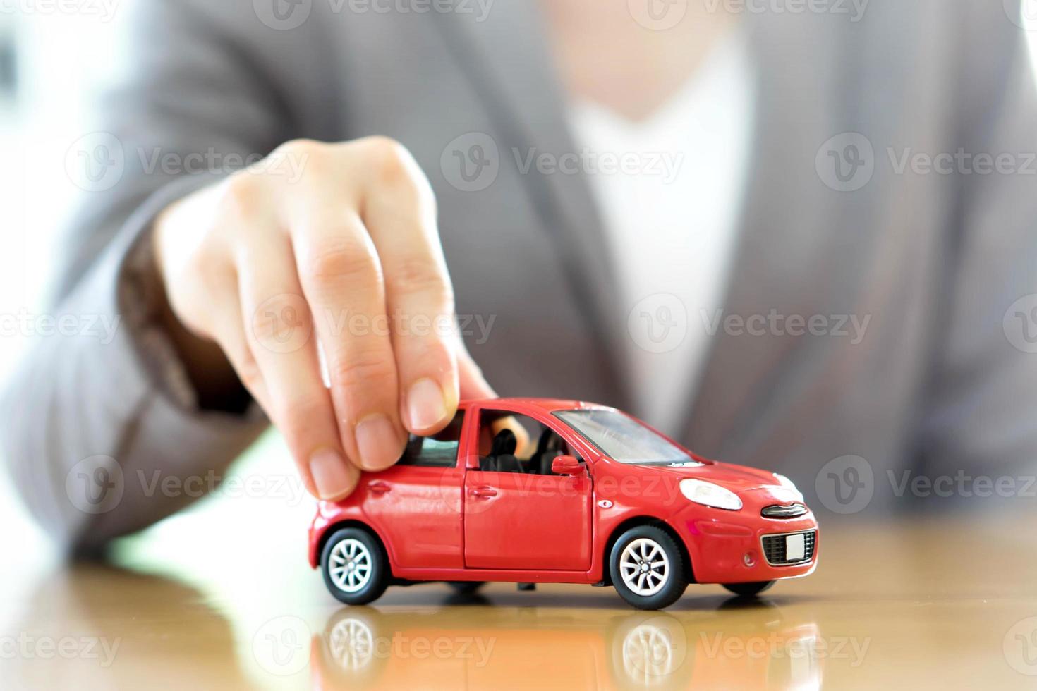 mulher de negócios por uma mesa segurando um carro de brinquedo. foto