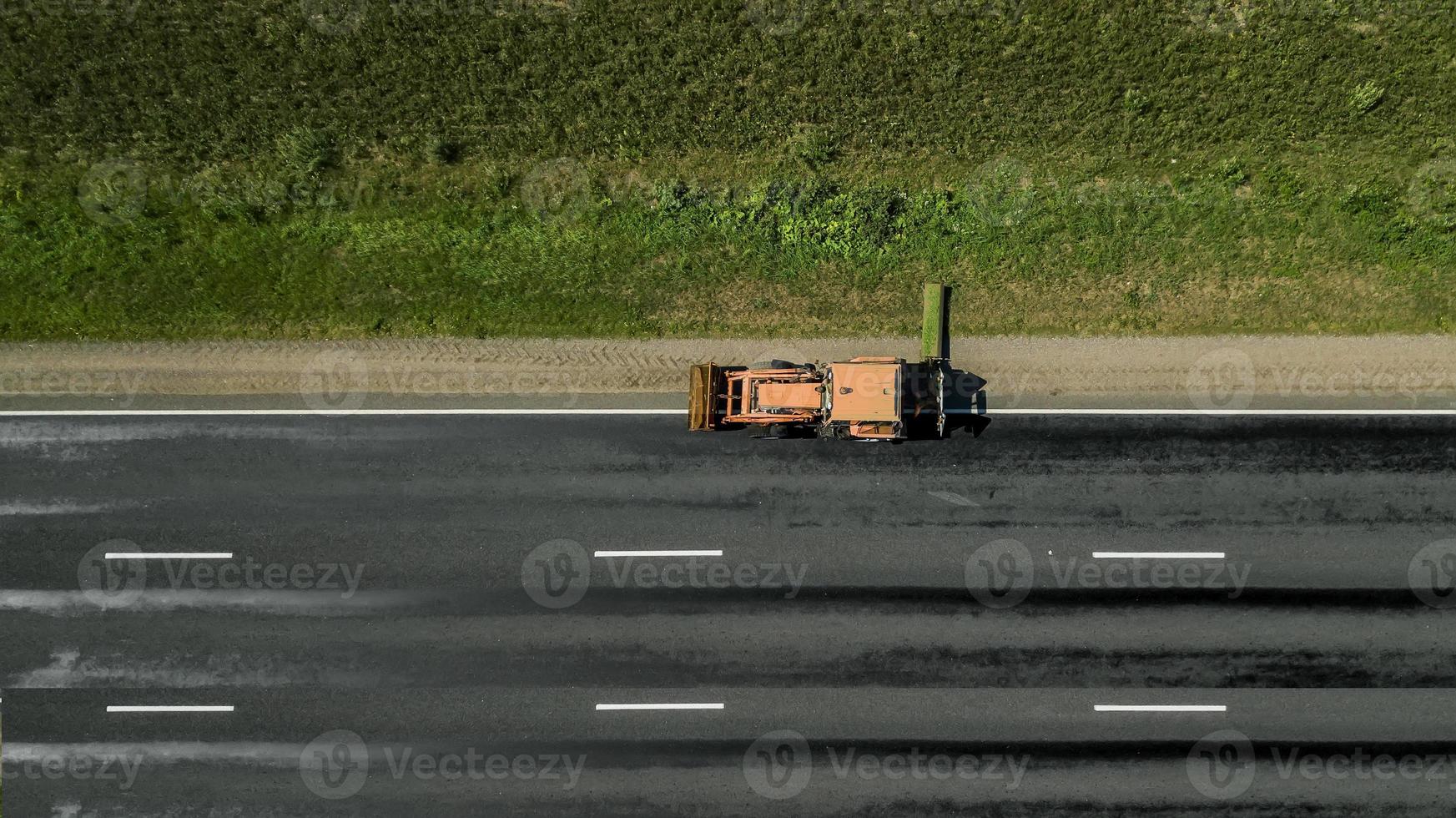 trator corta a beira da estrada ao longo da estrada vista aérea foto