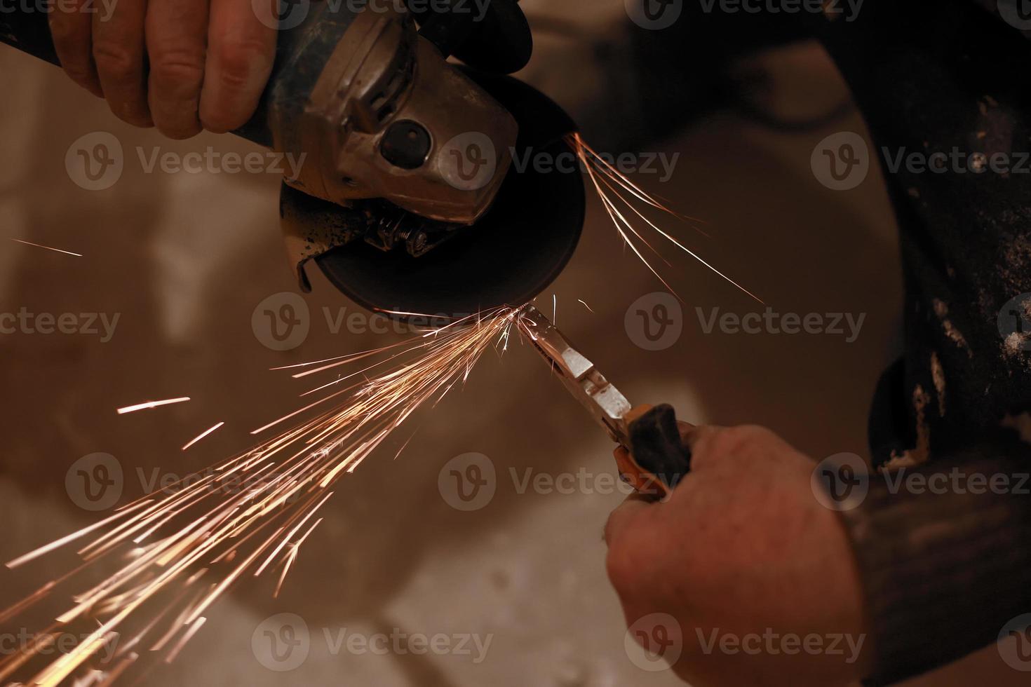 metalúrgico masculino polindo e finalizando. mãos de homem tratando peças metálicas de hardware em uma oficina com rebarbadora foto