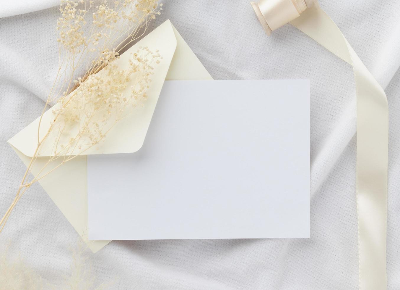 maquete de convite de cartão em branco 5x7 no envelope com flores secas e fita em fundo de papel, postura plana, maquete foto