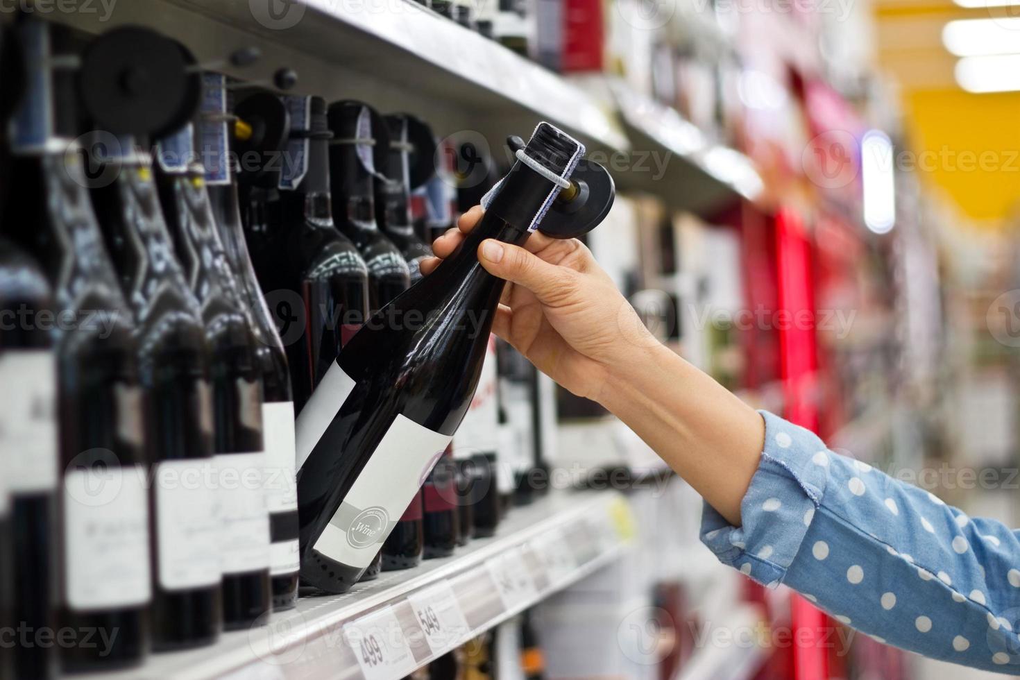 mulher está comprando uma garrafa de vinho no fundo do supermercado foto