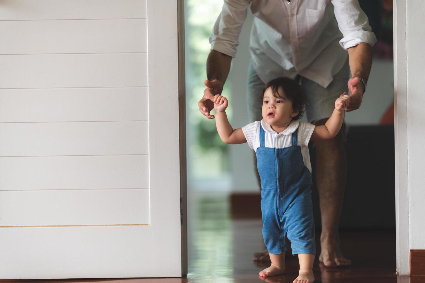 criança bonitinha conceito de família criança, bebê aprendendo a andar com pai e mãe para ajudar a cuidar e segurar a mão, primeiro passo com apoio dos pais na infância, pequeno retrato de amor menino em casa foto