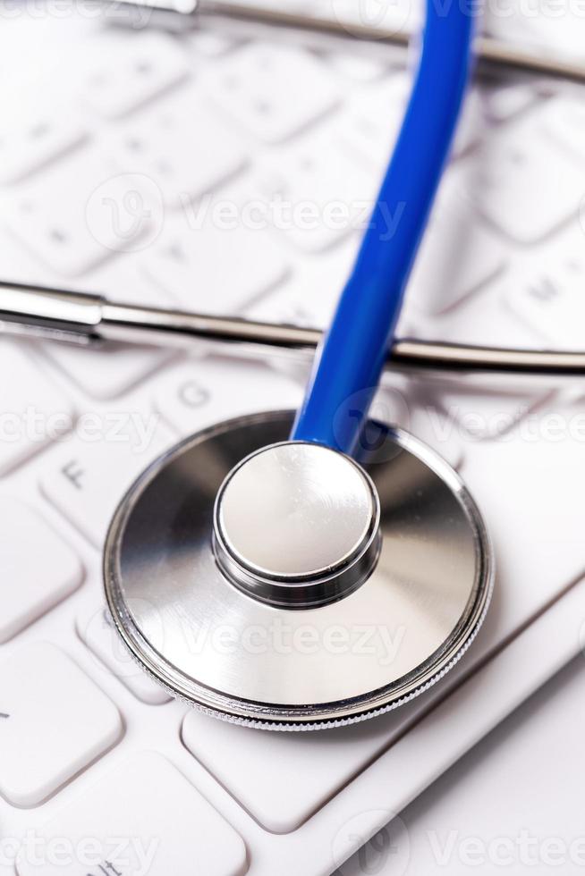 estetoscópio azul no teclado do computador no fundo da mesa branca. conceito de tecnologia de tratamento de informações médicas on-line, close-up, macro, copie o espaço foto