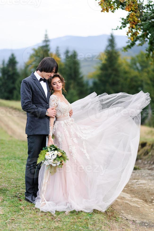 a noiva e o noivo estão abraçando sob um velho carvalho. sessão de fotos de casamento nas montanhas.