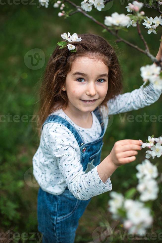 uma menina bonitinha de 5 anos em um pomar de maçãs brancas florescendo na primavera. primavera, pomar, floração, alergia, fragrância primaveril, ternura, cuidado com a natureza. retrato foto